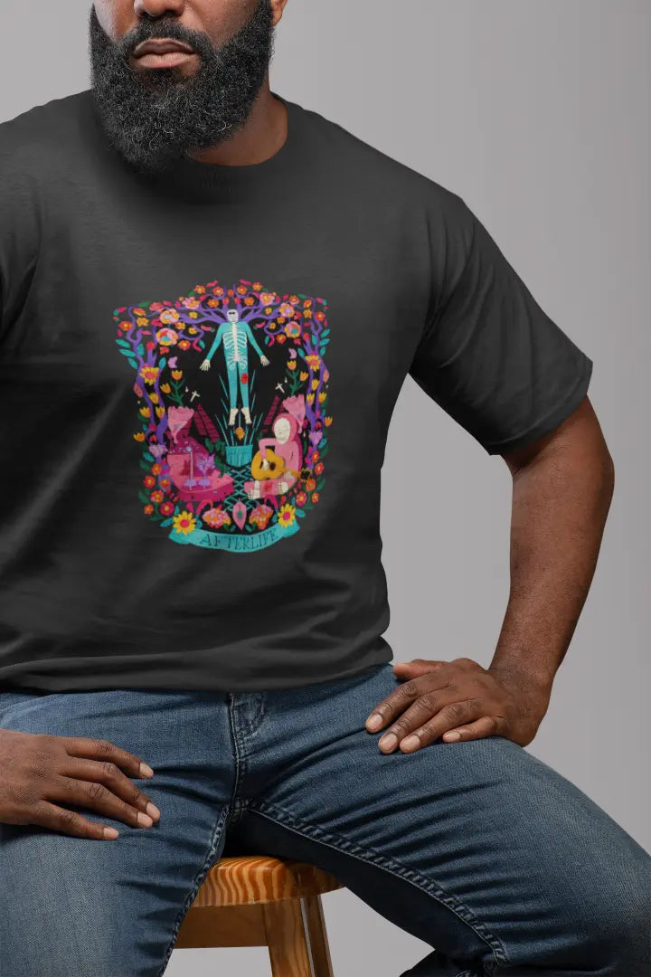 Bearded man sitting on a wooden stool, wearing a black aesthetic T-shirt featuring a psychedelic graphic design with a colorful floral pattern, set against a light grey background.