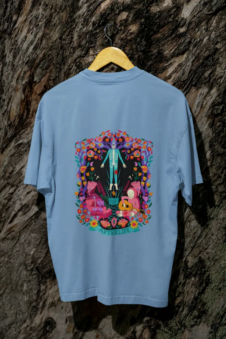 Baby Blue back printed oversized tee shirt for men hanging on a wooden hanger against a textured background, featuring a colorful psychedelic illustration of two figures—one standing and the other sitting on a bench surrounded by flowers and leaves in vibrant, intricate detail.