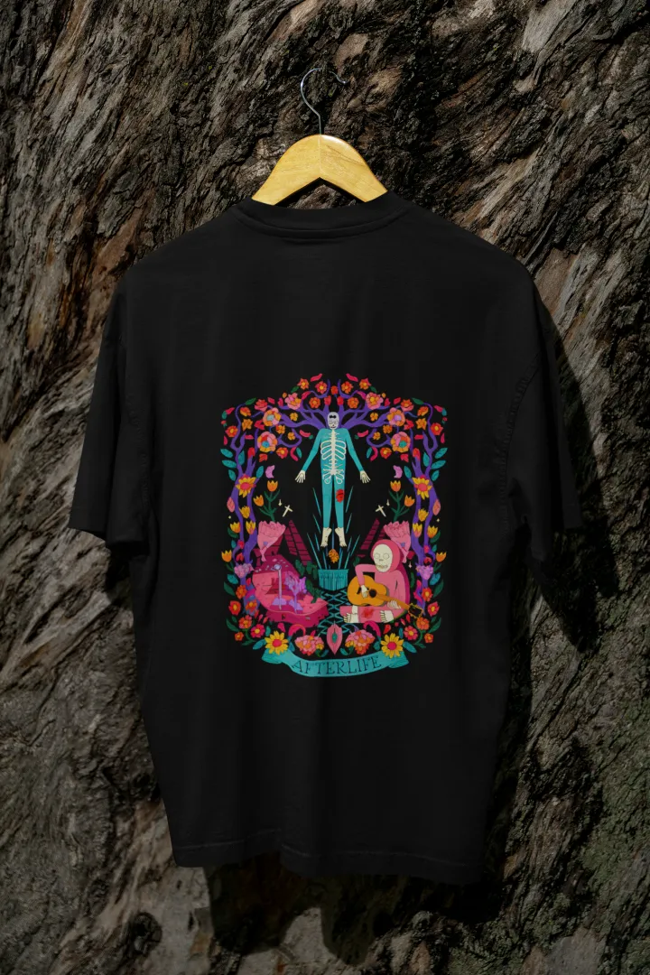 Black back printed oversized tee shirt for men hanging on a wooden hanger against a textured background, featuring a colorful psychedelic illustration of two figures—one standing and the other sitting on a bench surrounded by flowers and leaves in vibrant, intricate detail.