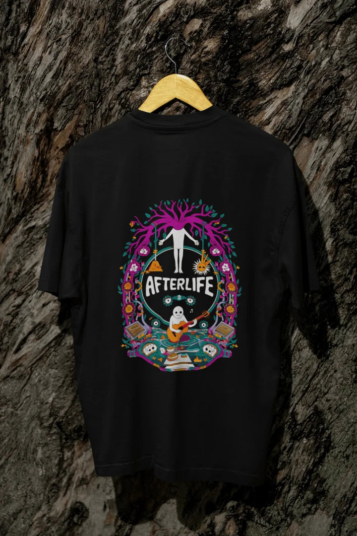 Black oversized tee shirt hanging on a wooden hanger against a textured background, featuring a colorful psychedelic circular design with the word 'Afterlife' at the top. The design includes a tree with pink and purple leaves, and a skull and crossbones, surrounded by vibrant, intricate details.