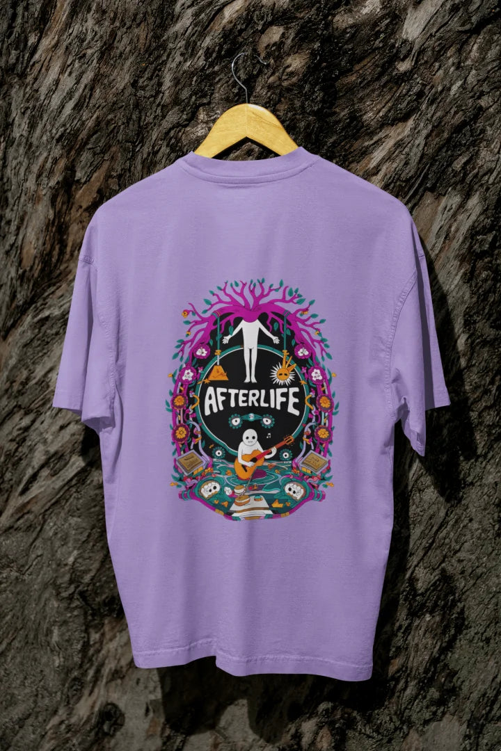 Lavender oversized tee shirt hanging on a wooden hanger against a textured background, featuring a colorful psychedelic circular design with the word 'Afterlife' at the top. The design includes a tree with pink and purple leaves, and a skull and crossbones, surrounded by vibrant, intricate details.