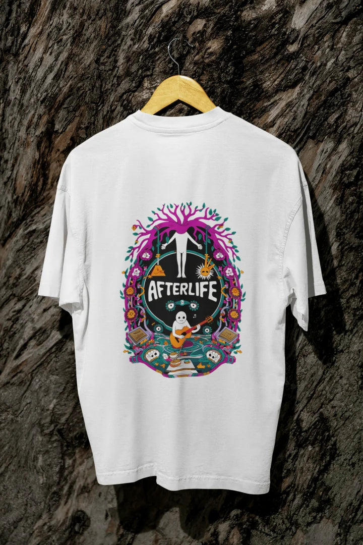 White oversized tee shirt hanging on a wooden hanger against a textured background, featuring a colorful psychedelic circular design with the word 'Afterlife' at the top. The design includes a tree with pink and purple leaves, and a skull and crossbones, surrounded by vibrant, intricate details.