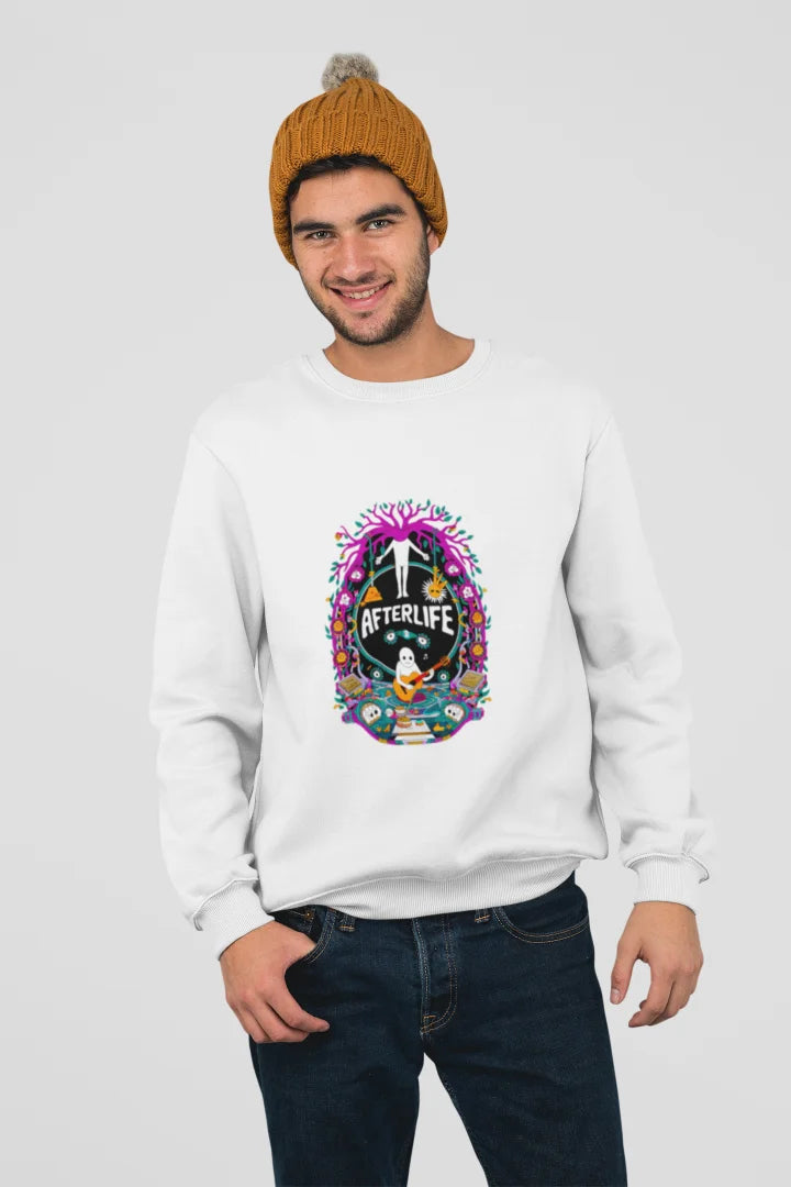 Young man wearing a white sweatshirt with a colorful graphic design of a skull and the word Afterlife above it, surrounded by a pink and purple floral pattern. He is wearing a mustard-colored beanie and blue jeans, standing with his hands in his pockets and smiling at the camera against a plain white background.