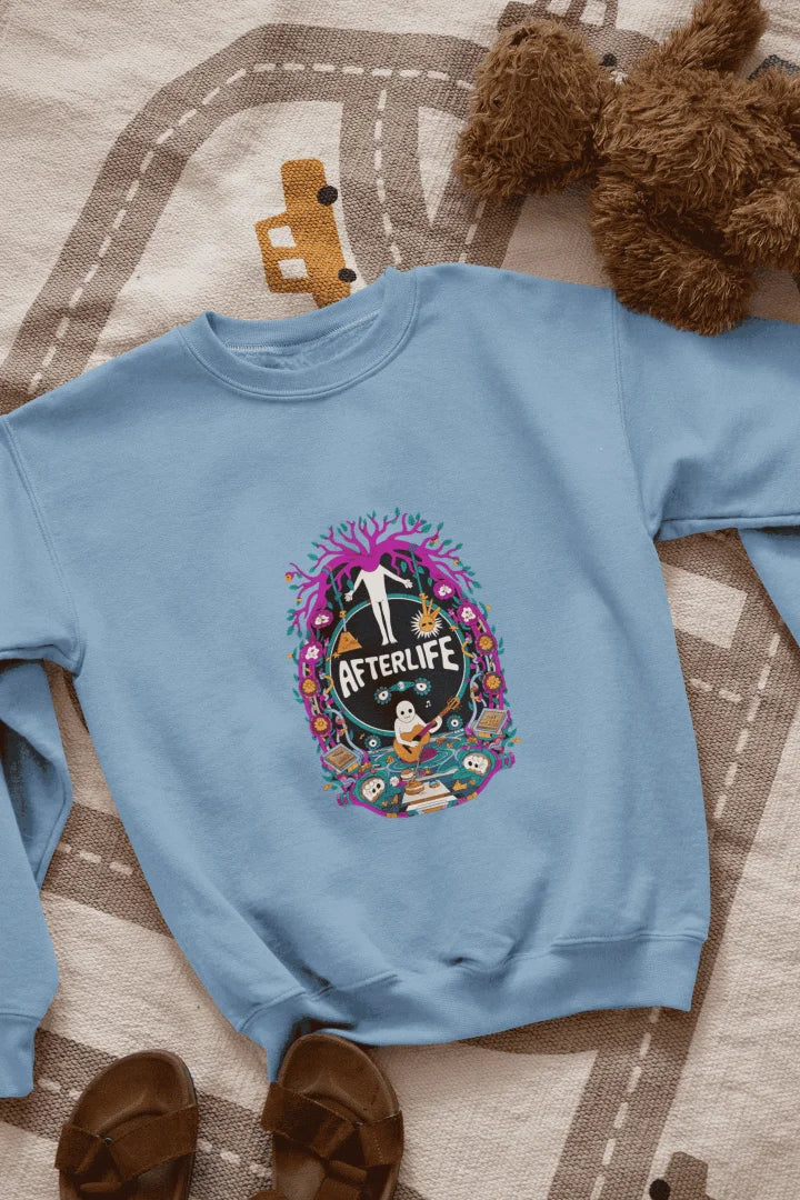 Blue sweatshirt featuring a colorful graphic design with a circular Afterlife text, showing a person with outstretched arms standing in front of a tree with pink and purple leaves. The design includes a light blue sky with white clouds, a person in a blue shirt smiling, and brown sandals and a teddy bear on a beige and white patterned blanket.