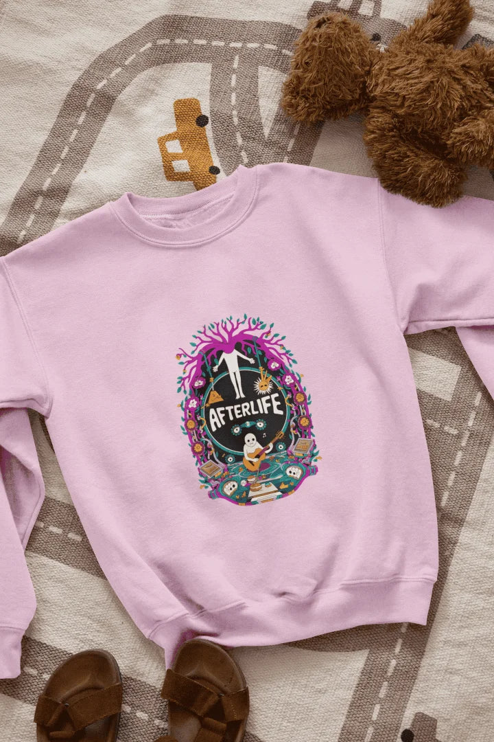 Light Pink sweatshirt featuring a colorful graphic design with a circular Afterlife text, showing a person with outstretched arms standing in front of a tree with pink and purple leaves. The design includes a light blue sky with white clouds, a person in a blue shirt smiling, and brown sandals and a teddy bear on a beige and white patterned blanket.