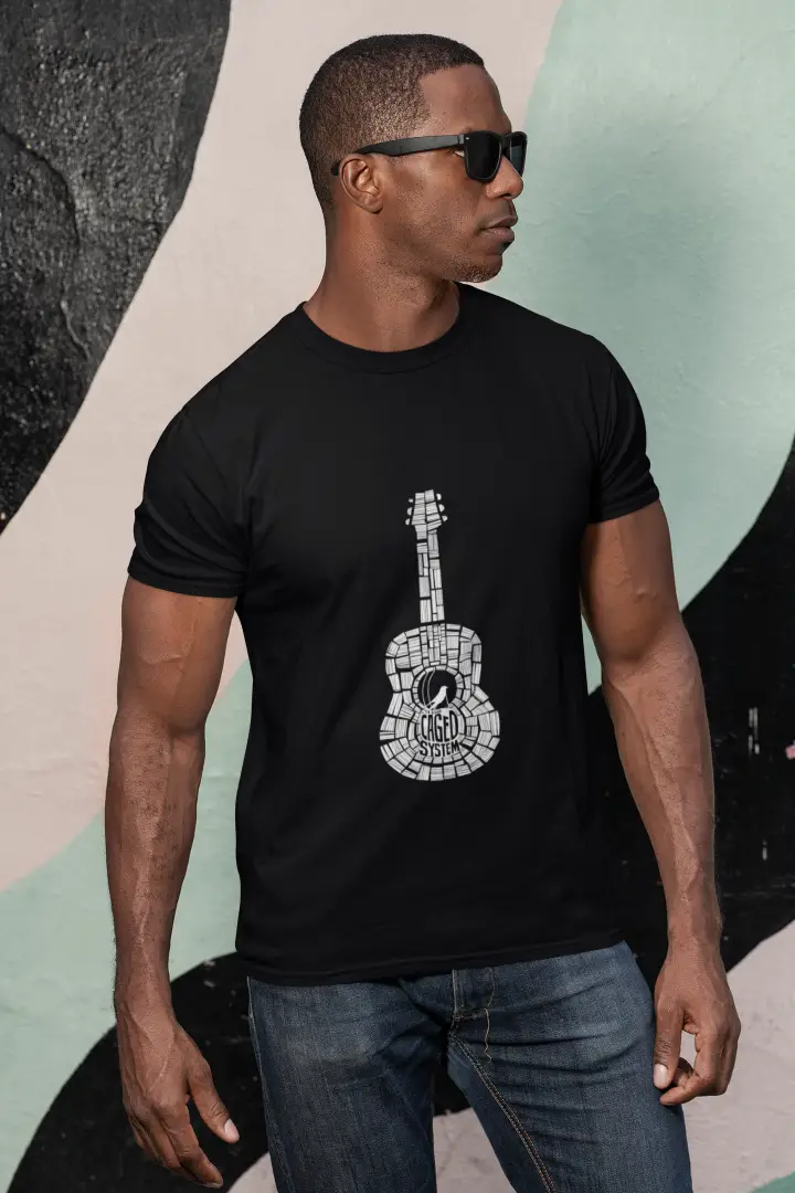 Young man wearing a black T-shirt with a white minimal guitar graphic design, dark sunglasses, and blue jeans. He is standing in front of a colorful abstract background with a serious expression.