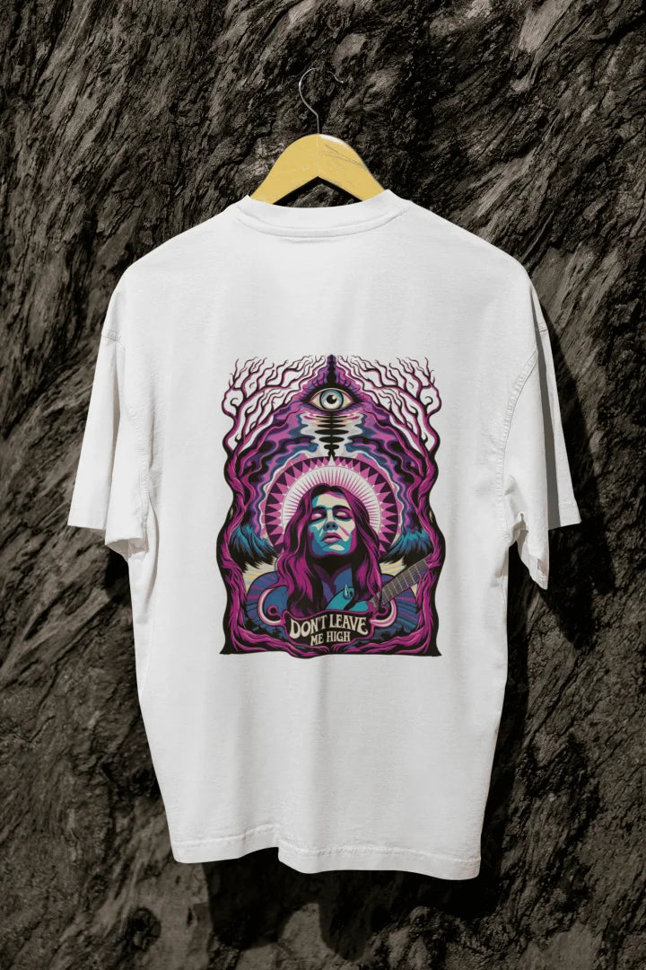 A white t-shirt with a graphic design featuring a woman with purple hair playing a guitar, surrounded by mystical foliage and an eye. The design includes the text “DON’T LEAVE ME HIGH” in bold, psychedelic colors like purple, blue, and pink.