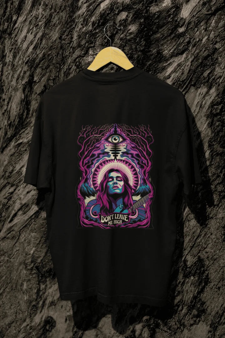A black oversized t-shirt with a graphic design featuring a woman with purple hair playing a guitar, surrounded by mystical foliage and an eye. The design includes the text “DON’T LEAVE ME HIGH” in bold, psychedelic colors like purple, blue, and pink.