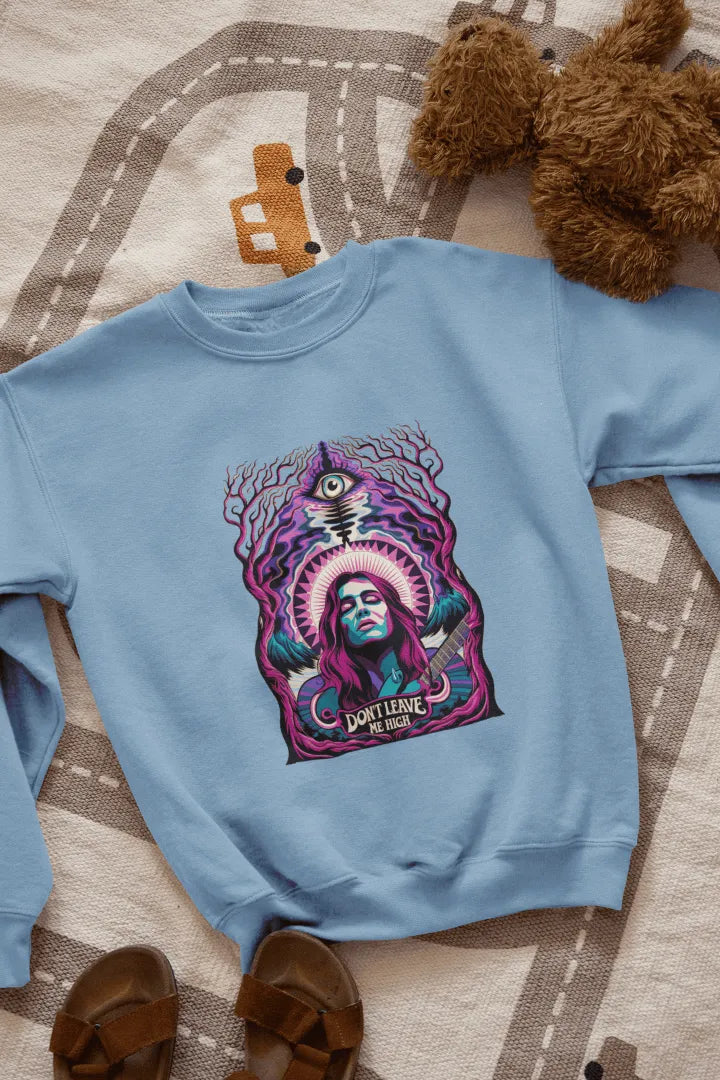 A blue sweatshirt with a graphic design. Centered on the front is a stylized portrait of a woman with long purple hair, holding a guitar. She has a confident expression, and the design features vibrant purple, teal, and pink hues, with a surreal forest-like background of dark purple and teal trees. A stylized eye and the text “Don’t Leave Me High” are visible beneath her.