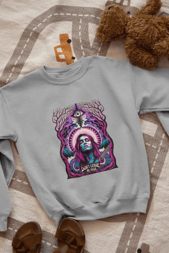 A grey sweatshirt with a graphic design. Centered on the front is a stylized portrait of a woman with long purple hair, holding a guitar. She has a confident expression, and the design features vibrant purple, teal, and pink hues, with a surreal forest-like background of dark purple and teal trees. A stylized eye and the text “Don’t Leave Me High” are visible beneath her.
