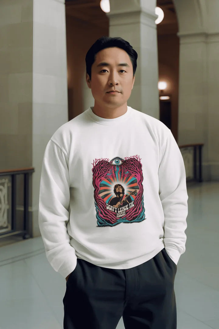 A man of Asian descent is centred in the image, wearing a white crew-neck sweatshirt with a vibrant psychedelic graphic. The design features a musician with the words “Don’t Leave Me Hush” in shades of magenta, teal, and orange. He has short, dark hair and a neutral expression, standing in black pants.