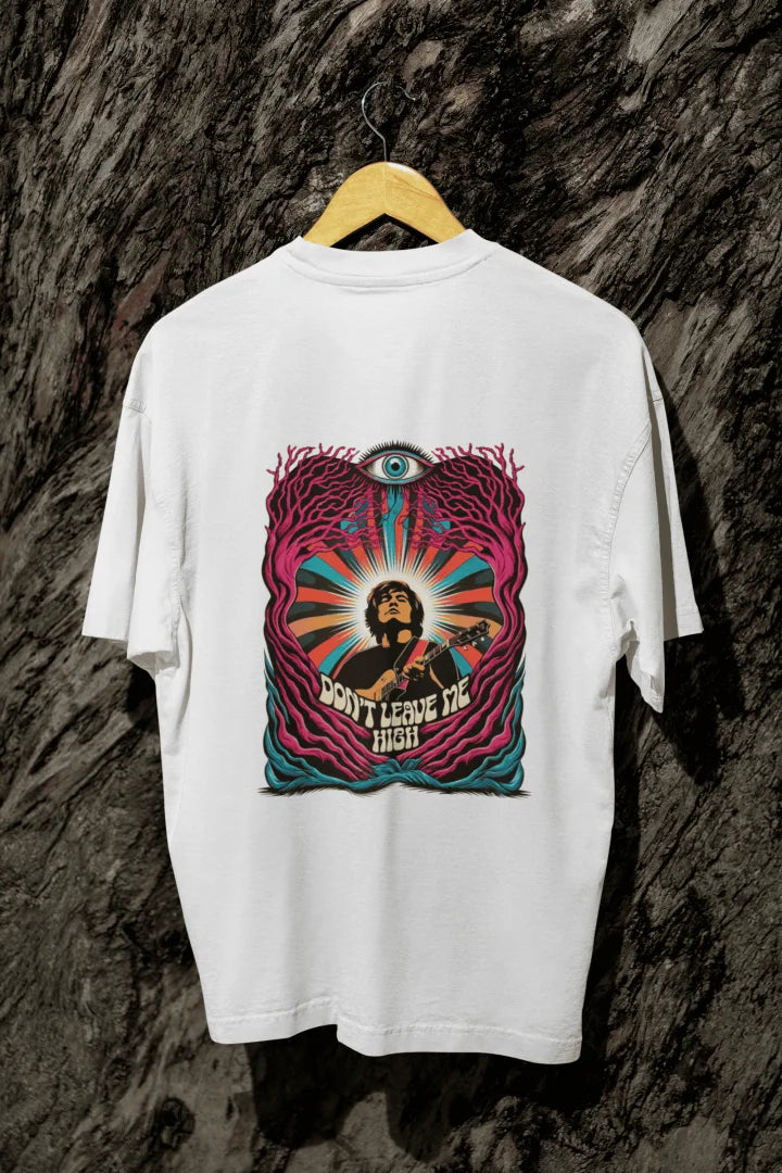 A white oversized t-shirt with a psychedelic graphic on the back, featuring a musician playing a guitar surrounded by vibrant swirling colors. The design includes a large stylized eye and the text “DON’T LEAVE ME HIGH,” evoking a 1960s/1970s psychedelic art style. The composition is centred, with harmonious lighting and a visually impactful atmosphere.