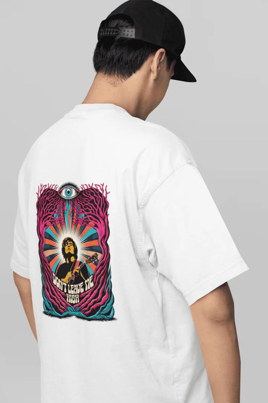 A man wearing white oversized t-shirt with a back graphic design of a man playing guitar, surrounded by vibrant pink, teal, and orange swirling trees or vines. The text “DON’T LEAVE ME HIGH” is underneath. The design has a psychedelic, artistic style with bold colors and intricate details.