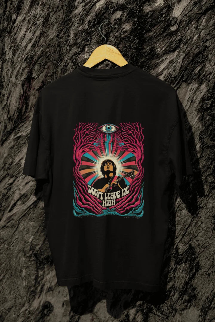 A black oversized t-shirt with a psychedelic graphic on the back, featuring a musician playing a guitar surrounded by vibrant swirling colors. The design includes a large stylized eye and the text “DON’T LEAVE ME HIGH,” evoking a 1960s/1970s psychedelic art style. The composition is centered, with harmonious lighting and a visually impactful atmosphere.
