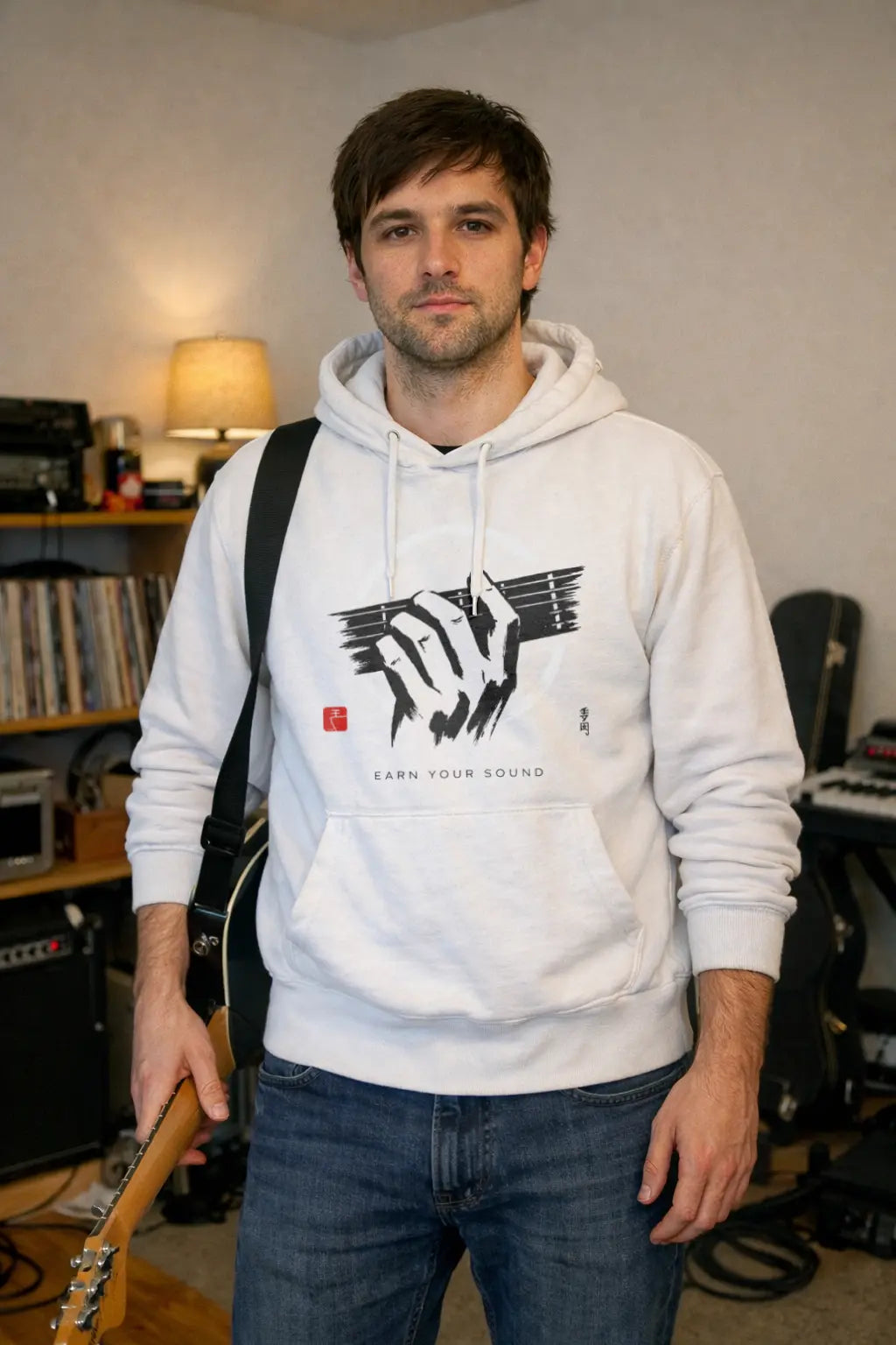 Man wearing a white hoodie with a graphic design in a room with musical equipment.