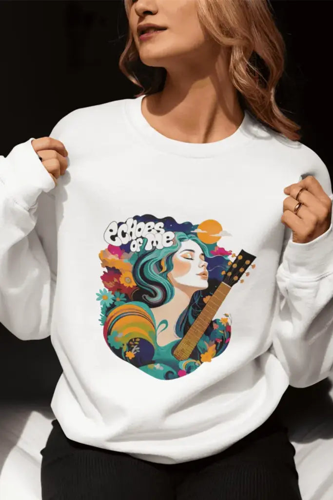 A white sweatshirt with a vibrant graphic of a woman with teal-green hair playing an acoustic guitar. Surrounded by colorful flowers, swirls, and text reading “Echoes of Me,” the design has a 1970s-inspired artistic style with teal, orange, and purple hues. Whimsical and stylish.