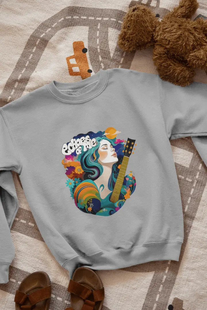 A grey sweatshirt with a vibrant graphic of a woman with flowing teal hair holding a guitar, surrounded by floral and swirling patterns in teal, orange, and cream tones. The text “Echoes of Me” appears above the design, evoking a 1960s-70s aesthetic. Soft and calming atmosphere.