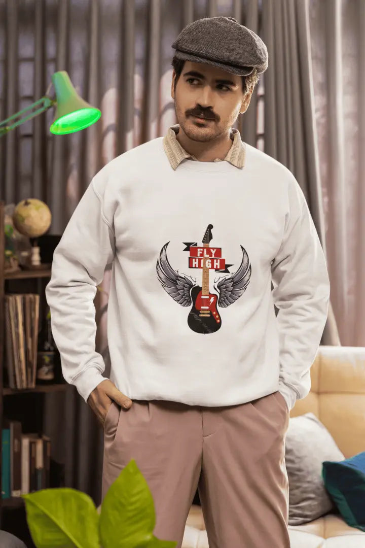A white sweatshirt featuring a graphic design of a black electric guitar with gray wings and “FLY HIGH” on a red banner. The man, in light brownish-pink pants and a gray newsboy cap, is standing in a room with a bookshelf, green lamp, and plants in the background.