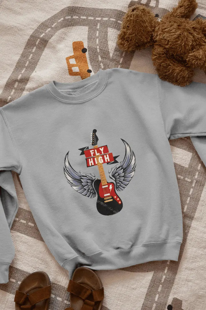 A grey sweatshirt with a graphic design of a black electric guitar with gray and white angel wings, and a red “FLY HIGH” banner. The sweatshirt is laid flat on a light beige road-patterned rug, with brown leather sandals at the bottom left. Soft lighting highlights the graphic, creating a relaxed, casual atmosphere.