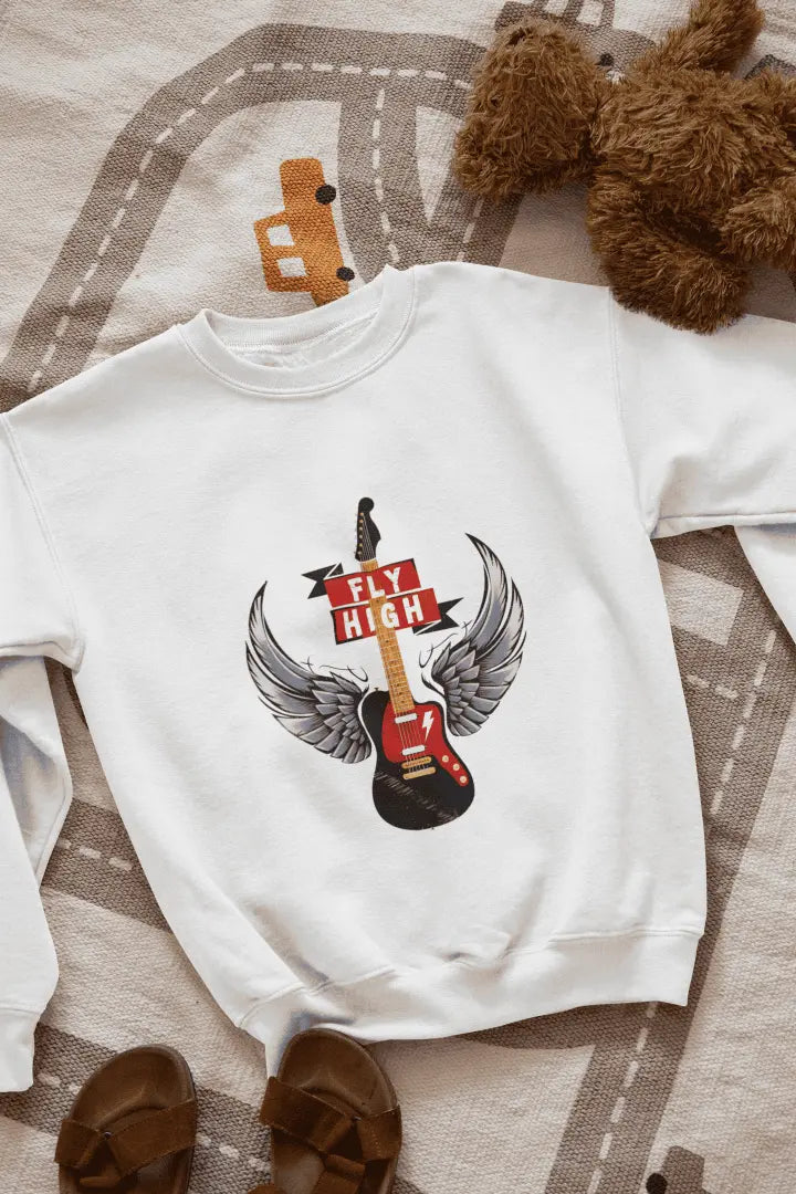 A white sweatshirt with a graphic design of a black electric guitar with gray and white angel wings, and a red “FLY HIGH” banner. The sweatshirt is laid flat on a light beige road-patterned rug, with brown leather sandals at the bottom left. Soft lighting highlights the graphic, creating a relaxed, casual atmosphere.