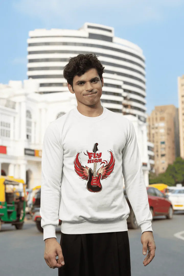 A man wearing a white sweatshirt with a red electric guitar and wings graphic, featuring the text “FLY HIGH.” He pairs it with black pants, standing confidently on a sunny city street with a beige building in the blurred background.