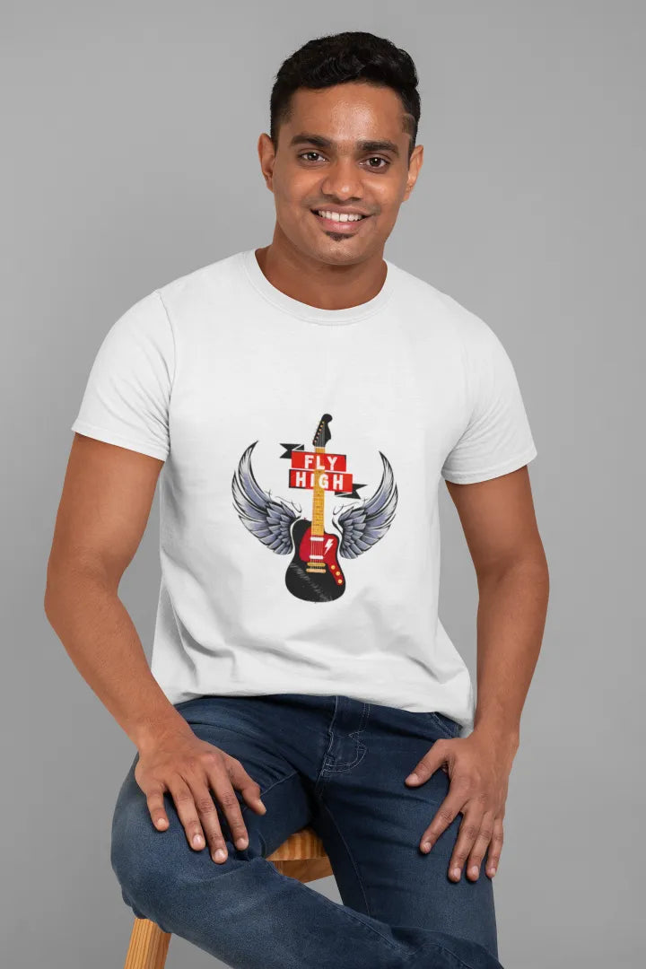 A man sitting on a chair wearing a white T-shirt with the design of a guitar having wings. There’s a text saying Fly High.