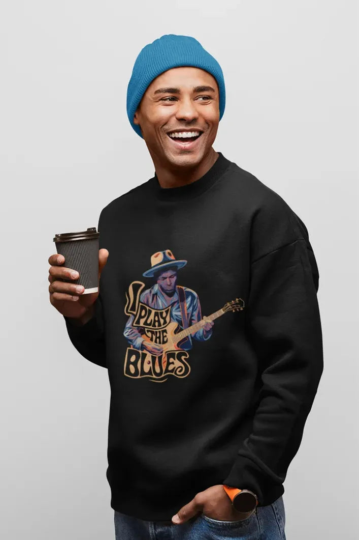 A man holding a coffee cup in his hand wearing a black sweatshirt with the design of a man playing guitar. There’s a text on the design saying I play the blues.