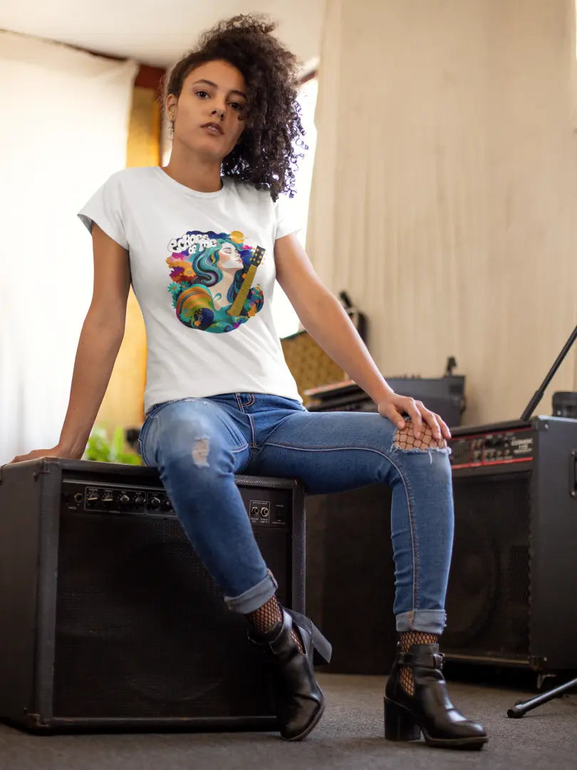 A girl with curly hair sitting on an amplifier wearing a white T-shirt. The T-shirt consists of a psychedelic design of a girl holding a guitar. There’s a text saying echoes of me.