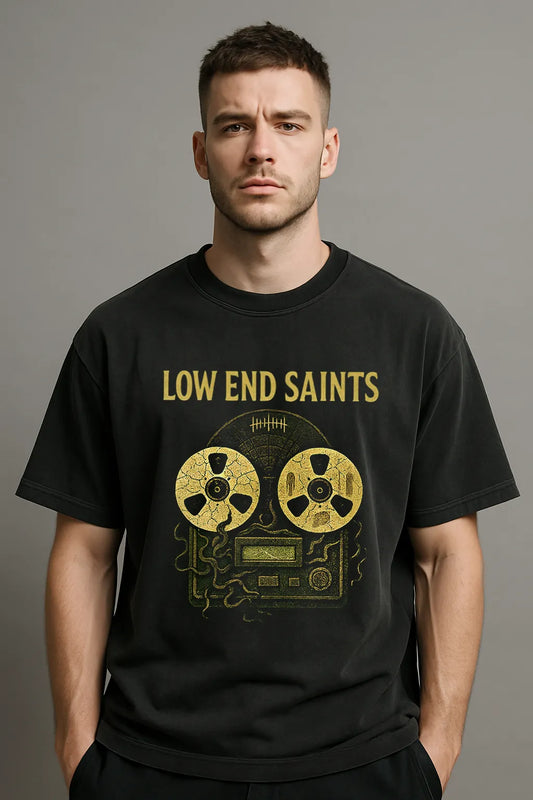 Man wearing a black 'Low End Saints' t-shirt with a reel-to-reel tape design on a gray background