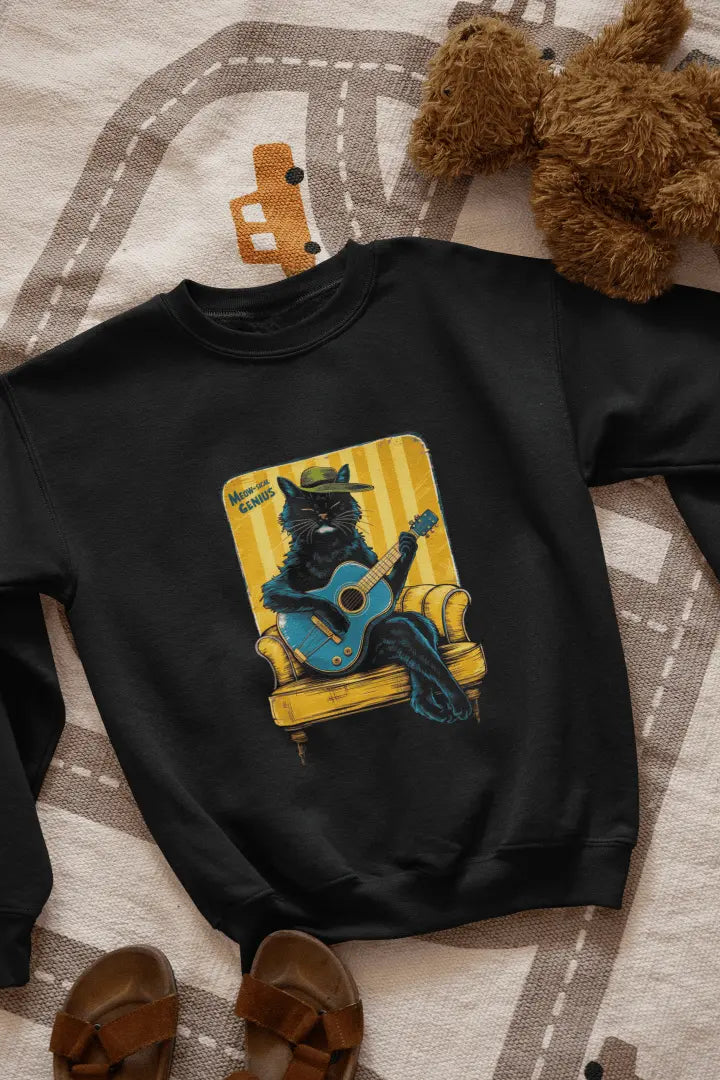 A black printed sweatshirt with the design of a cat wearing a cute cap and playing a guitar while sitting on a sofa. The sweatshirt is lying down on the floor. There’s a text saying meowsical genius.