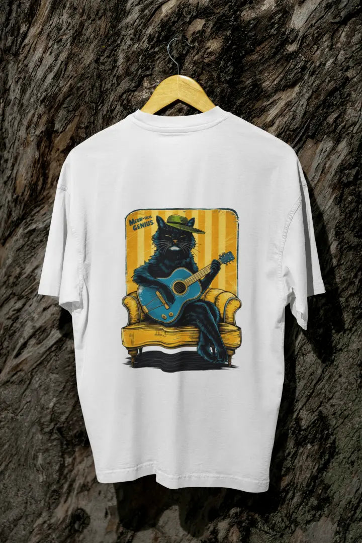 A white back printed oversized t-shirt with a back print hanging on a tree trunk. The print design contains a cat wearing a hat and sitting on the sofa. There's a text saying Meowsical Genius on the top left of the design.