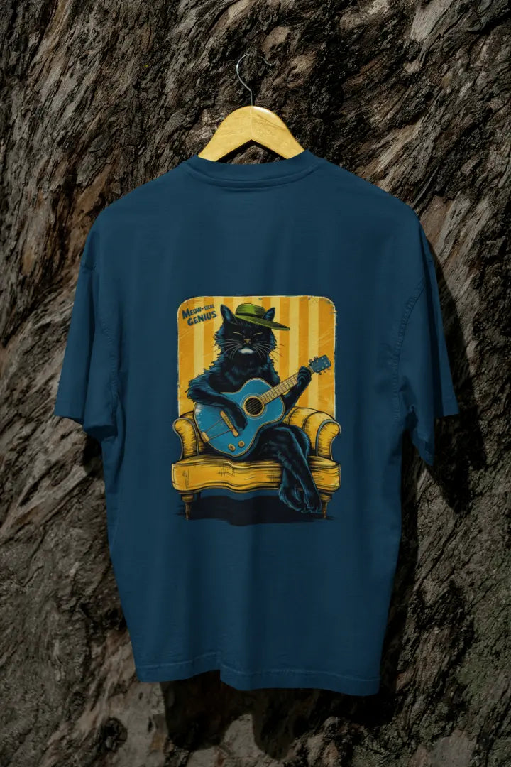A navy blue back printed oversized t-shirt with a back print hanging on a tree trunk. The print design contains a cat wearing a hat and sitting on the sofa. There's a text saying Meowsical Genius on the top left of the design.
