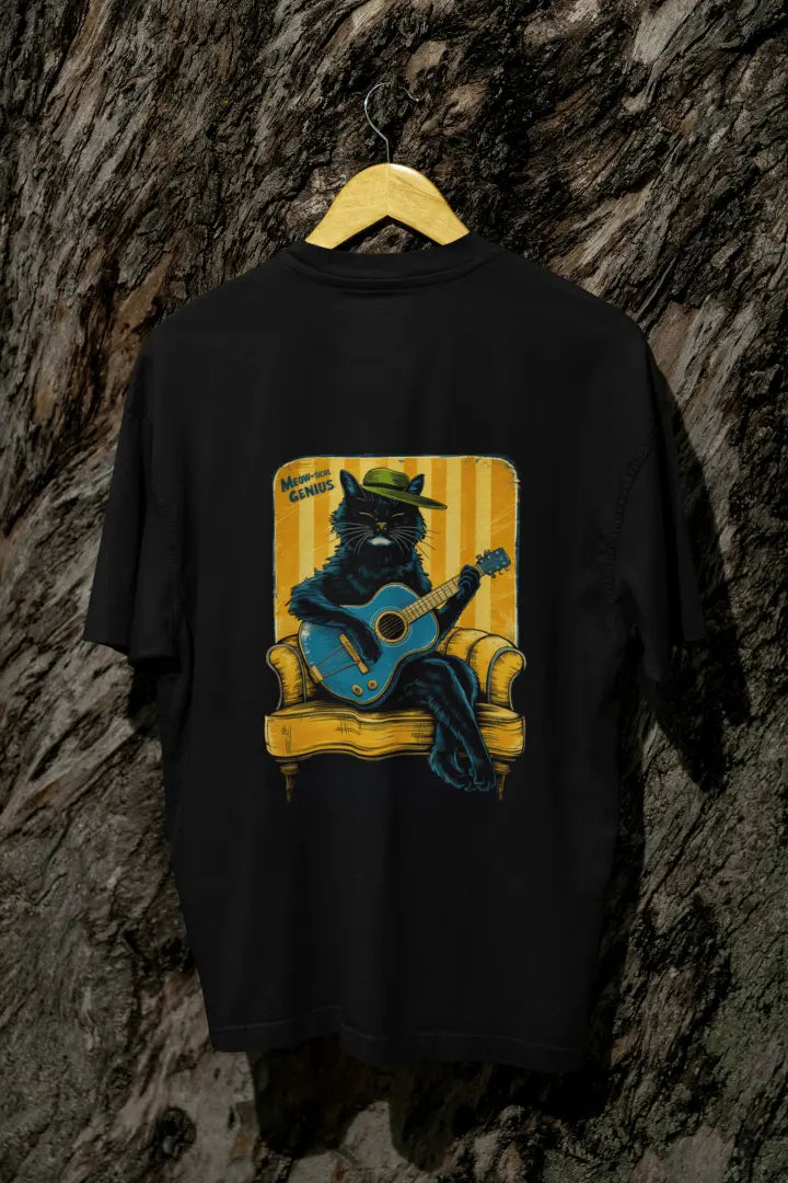 A black back printed oversized t-shirt with a back print hanging on a tree trunk. The print design contains a cat wearing a hat and sitting on the sofa. There's a text saying Meowsical Genius on the top left of the design.