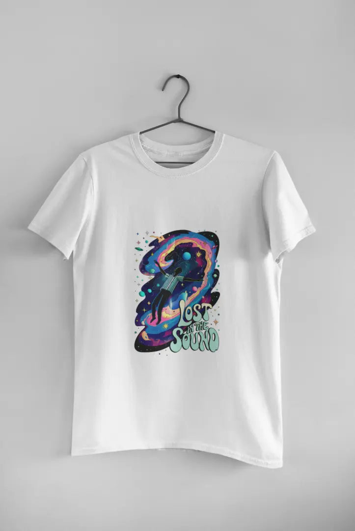 A white t-shirt with a design printed on the front hanging against a light grey wall. The design contains a man floating in space with planets and stars around him. There's a text saying Lost In The Sound at the bottom right of the design.