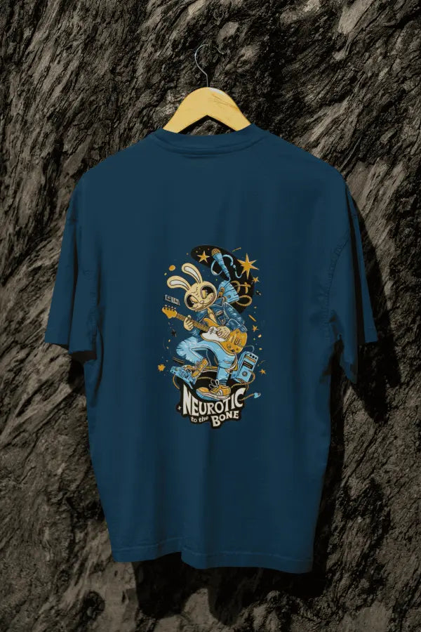 A navy blue oversized t-shirt with a design printed at the back hanging on a tree trunk. The design consists of a character playing a guitar. The overall design is funky. There's a text saying Neurotic to the Bone at the bottom of the design.