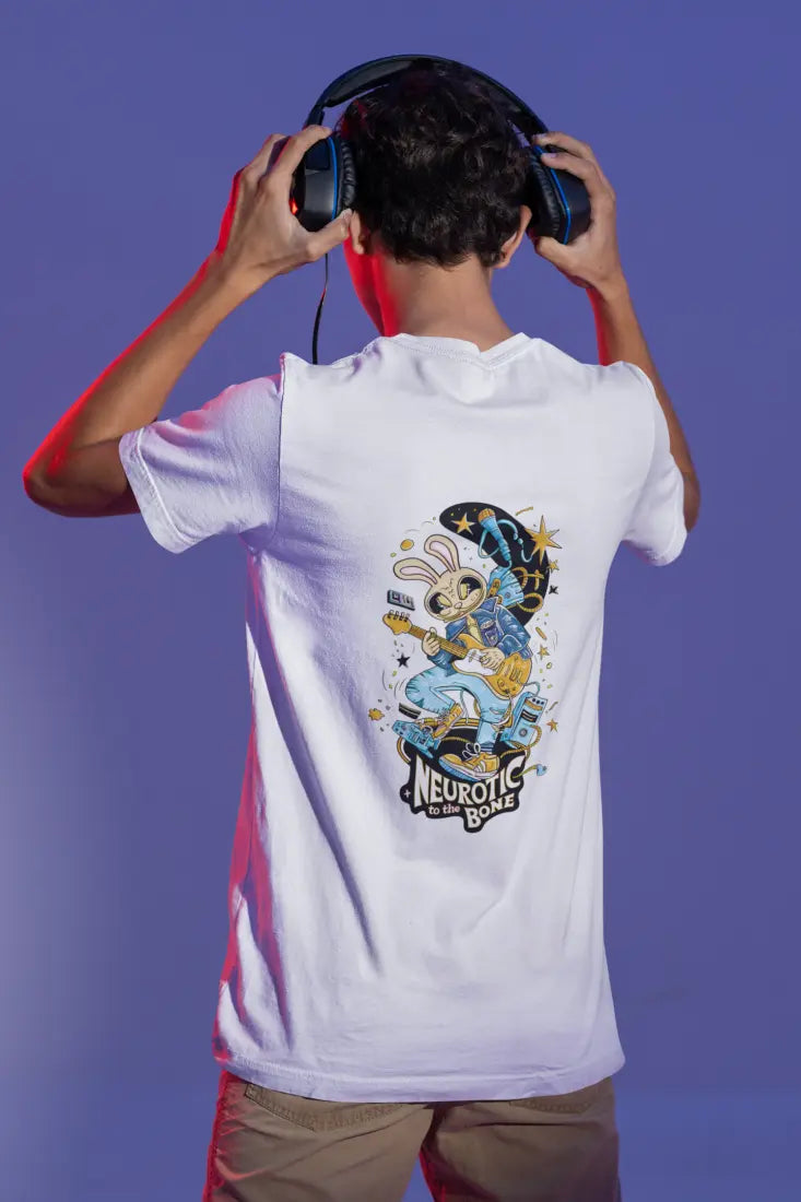 A young boy wearing a white oversized t-shirt with a design printed at the back. The design consists of a character playing a guitar. The overall design is funky. There's a text saying Neurotic to the Bone at the bottom of the design.