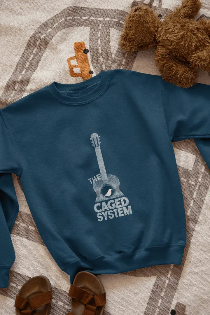 A navy blue sweatshirt with a minimal design printed on the front lying on the floor. The design consists of an acoustic guitar inside which a small bird is sitting. There's a text saying The Caged System at the bottom of the design.