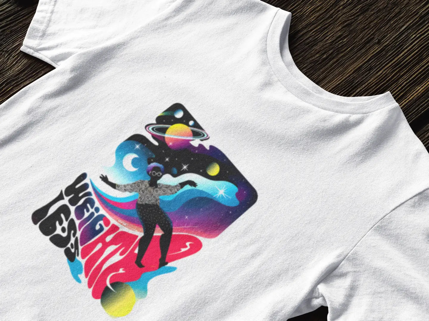 Close up of a white t-shirt with a design printed on the front. The design contains a woman who is floating in space with planets and stars around her. There's a text saying Weightless at the bottom of the design.