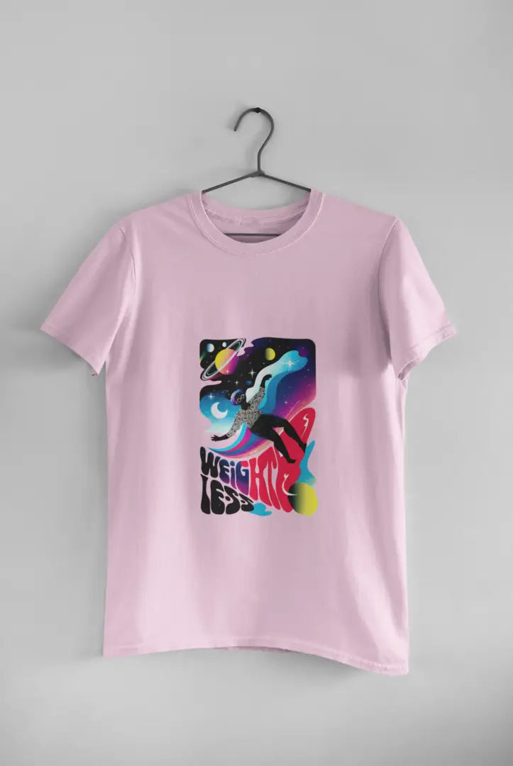 A pink t-shirt with a design printed on the front hanging against a light grey wall. The design contains a woman who is floating in space with planets and stars around her. There's a text saying Weightless at the bottom of the design.