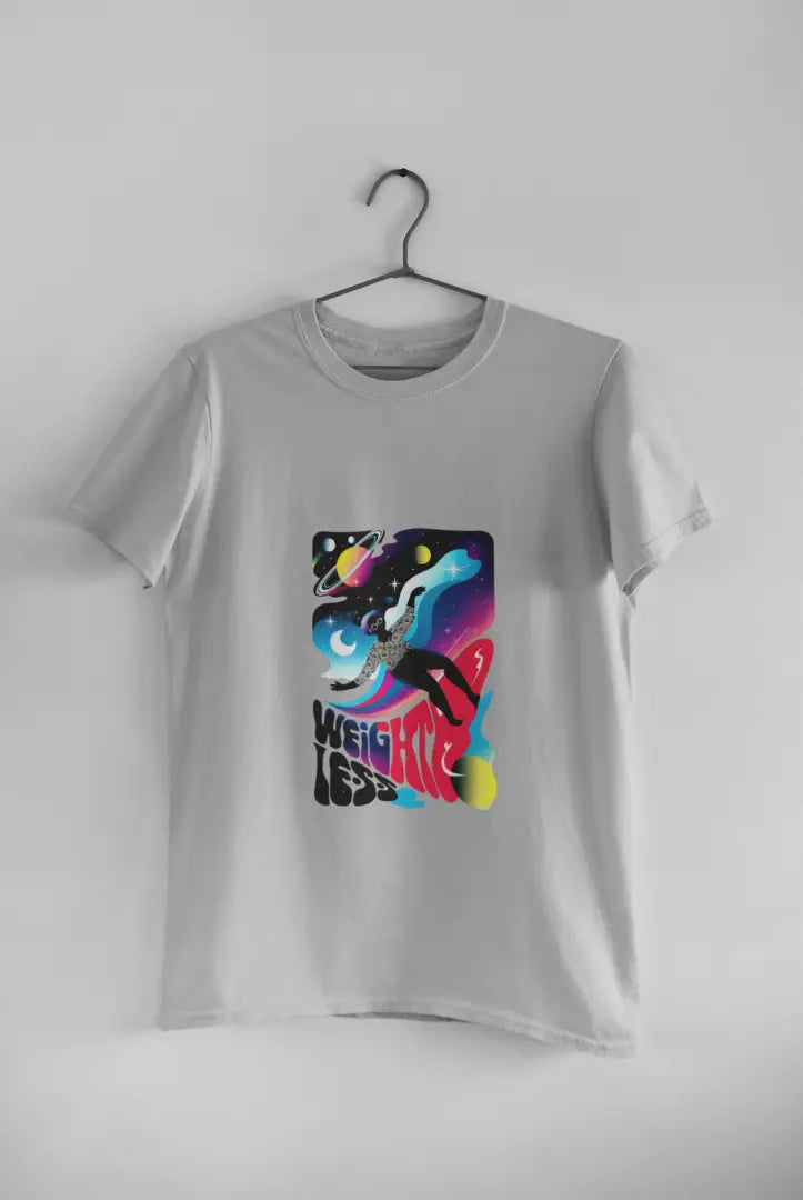 A grey t-shirt with a design printed on the front hanging against a light grey wall. The design contains a woman who is floating in space with planets and stars around her. There's a text saying Weightless at the bottom of the design.