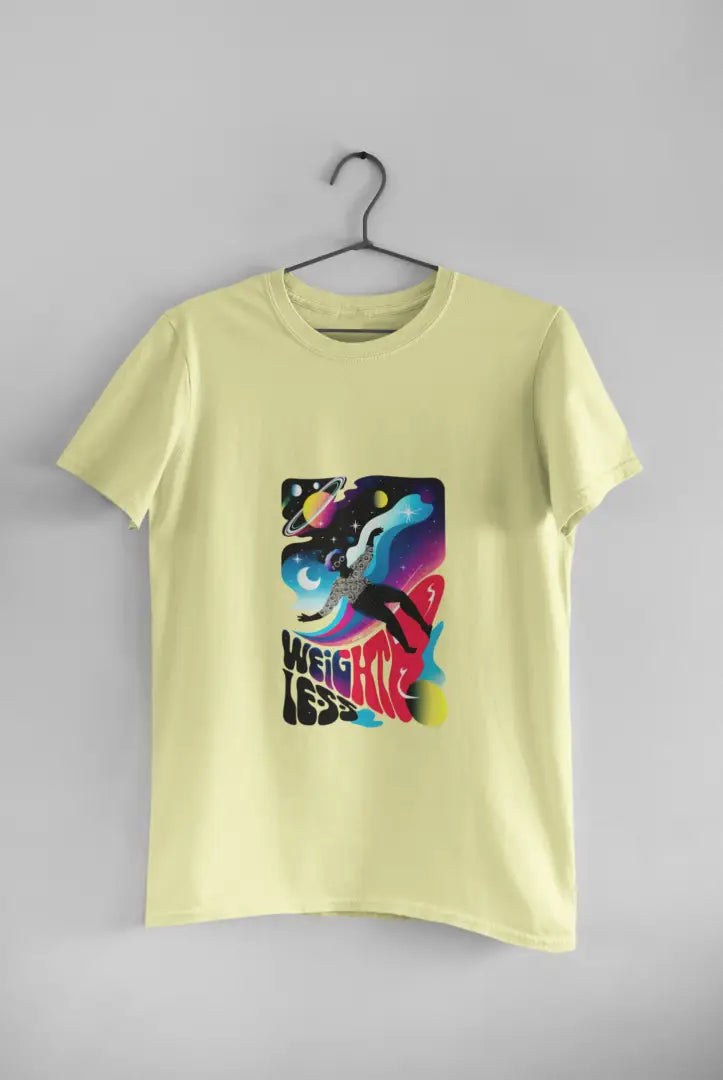 A yellow t-shirt with a design printed on the front hanging against a light grey wall. The design contains a woman who is floating in space with planets and stars around her. There's a text saying Weightless at the bottom of the design.