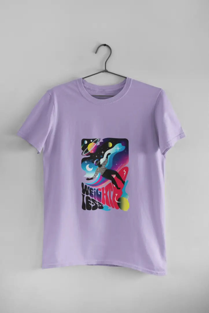 A lavender t-shirt with a design printed on the front hanging against a light grey wall. The design contains a woman who is floating in space with planets and stars around her. There's a text saying Weightless at the bottom of the design.
