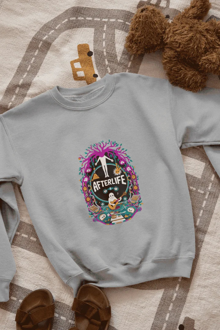 Grey sweatshirt featuring a colorful graphic design with a circular Afterlife text, showing a person with outstretched arms standing in front of a tree with pink and purple leaves. The design includes a light blue sky with white clouds, a person in a blue shirt smiling, and brown sandals and a teddy bear on a beige and white patterned blanket.
