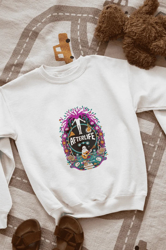 White sweatshirt featuring a colorful graphic design with a circular Afterlife text, showing a person with outstretched arms standing in front of a tree with pink and purple leaves. The design includes a light blue sky with white clouds, a person in a blue shirt smiling, and brown sandals and a teddy bear on a beige and white patterned blanket.