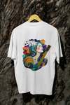 A white oversized T-shirt with a vibrant back graphic featuring a woman with teal-and-purple hair playing a golden guitar. Surrounded by colorful flowers, swirling patterns, and a crescent moon, the text “Echoes of Me” is integrated. The design has a 1970s-inspired psychedelic style, evoking a dreamy, musical vibe.