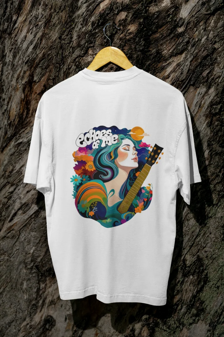 A white oversized T-shirt with a vibrant back graphic featuring a woman with teal-and-purple hair playing a golden guitar. Surrounded by colorful flowers, swirling patterns, and a crescent moon, the text “Echoes of Me” is integrated. The design has a 1970s-inspired psychedelic style, evoking a dreamy, musical vibe.