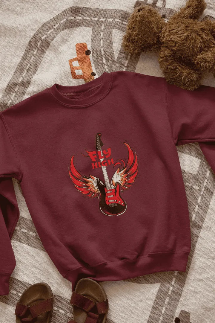 A maroon sweatshirt with a graphic design of a red electric guitar with fiery red wings, and the words “Fly High” in bold, red letters above it. The sweatshirt is laid flat on a beige-gray patterned rug with road markings, with brown sandals on either side. The lighting is soft and natural, giving the overall look a casual, fun style.