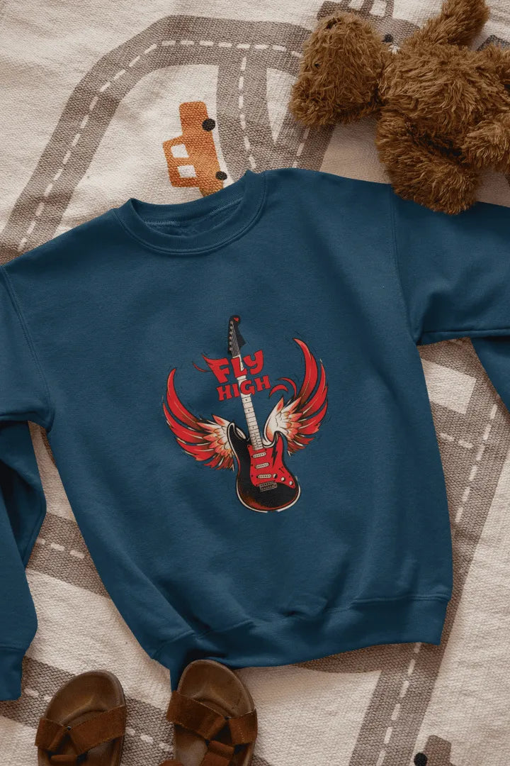 A navy blue sweatshirt with a graphic design of a red electric guitar with fiery red wings, and the words “Fly High” in bold, red letters above it. The sweatshirt is laid flat on a beige-gray patterned rug with road markings, with brown sandals on either side. The lighting is soft and natural, giving the overall look a casual, fun style.