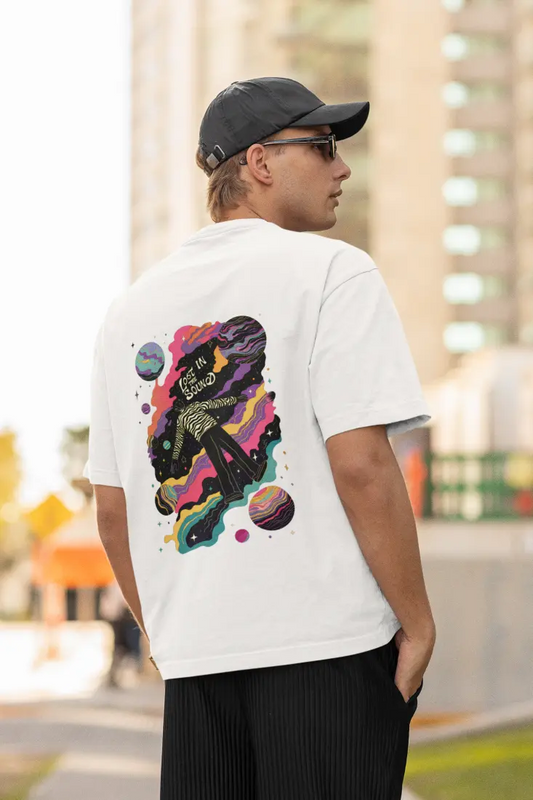 A man wearing a white oversized T-shirt with a back print of a man floating in space with planets and stars around him. There’s a text saying Lost In the sound at the top of the design.