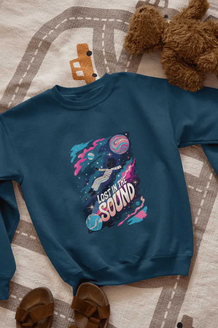 A printed navy blue sweatshirt lying on the floor with the design of a man floating in space. There’s a text saying Lost in the Sound.